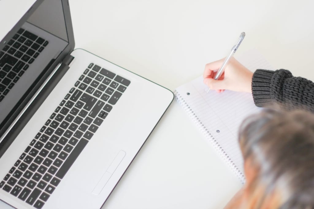 Photo of a woman writing a condo checklist in a notebook by her laptop.