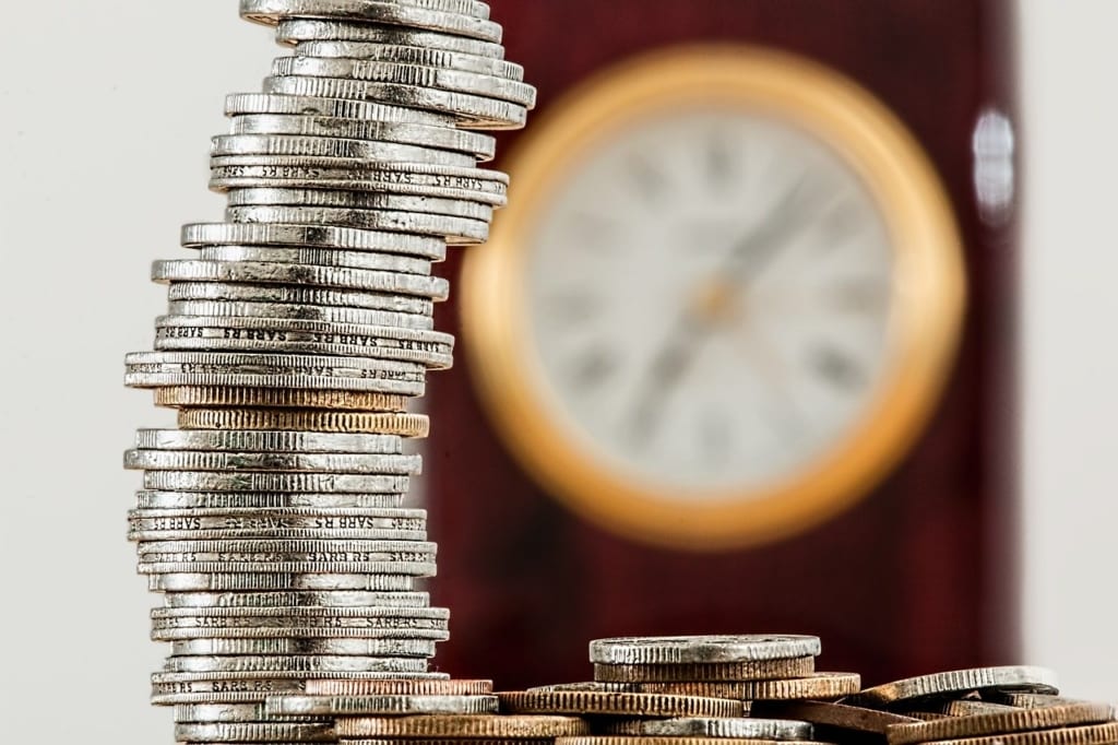A stack of coins with a blurry clock in the background.