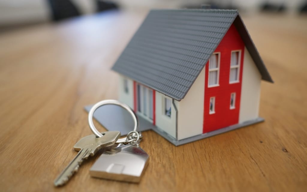Tiny model of a red and white house next to a set of keys.