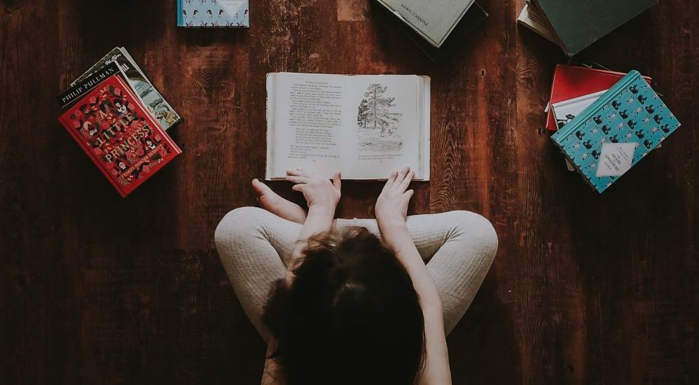 A child sitting on the floor reading books.