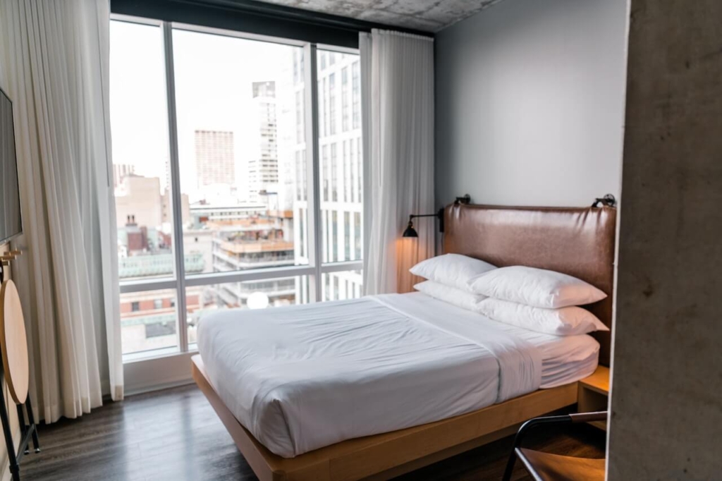 A white linen on the bed near the glass window with a view photo by Andrea Davis